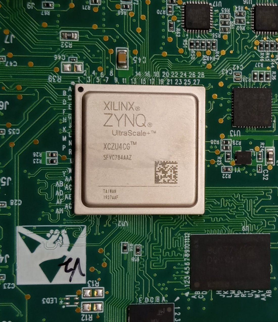 Układ Xilinx Zynq UltraScale+ w białej obudowie BGA wlutowany w zieloną płytkę drukowaną, z nadrukiem XCZU4CG i napisem Taiwan